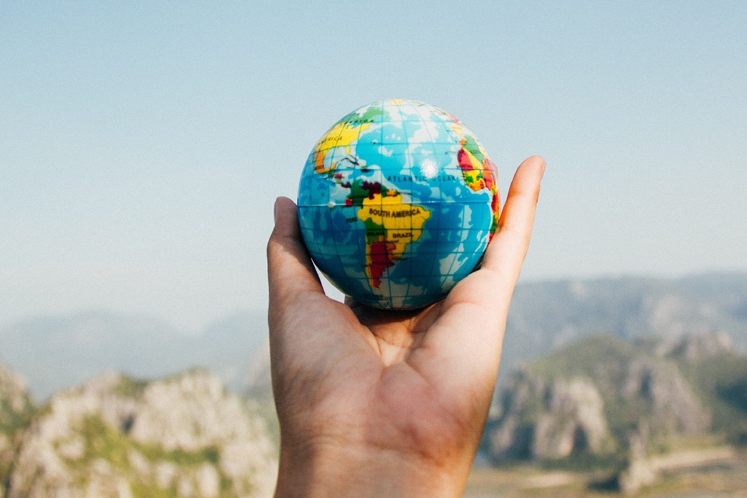 hand holds up a globe against background of mountains and the sky